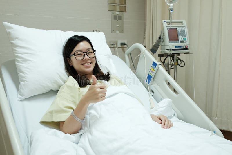 Asian patient girl thumbs up and smile while lying on hospital bed royalty free stock photos Asian patient girl thumbs up and smile while lying on hospital bed royalty free stock photos
