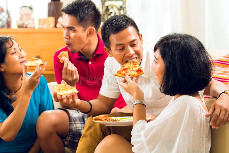 Asian people eating pizza at party or dinner and smiling