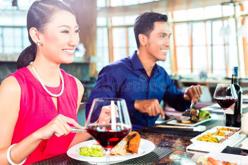 Asian people having dinner and drinking red wine in very fancy restaurant with open kitchen in background. Asian people having dinner and drinking red wine in very fancy restaurant with open kitchen in background