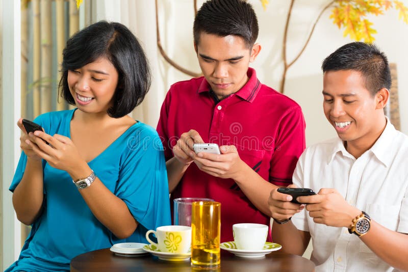 Asian people having fun together with mobile phone and drinking coffee or cocktail. Asian people having fun together with mobile phone and drinking coffee or cocktail