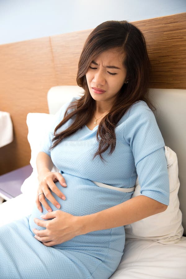 Asian Pregnant Woman Has Stomachache Sitting On Her Bed Stock Image