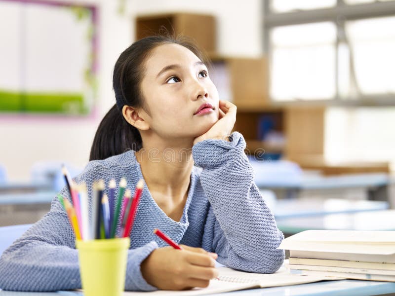 Asian elementary schoolgirl looking up and thinking while studying in classroom. Asian elementary schoolgirl looking up and thinking while studying in classroom.