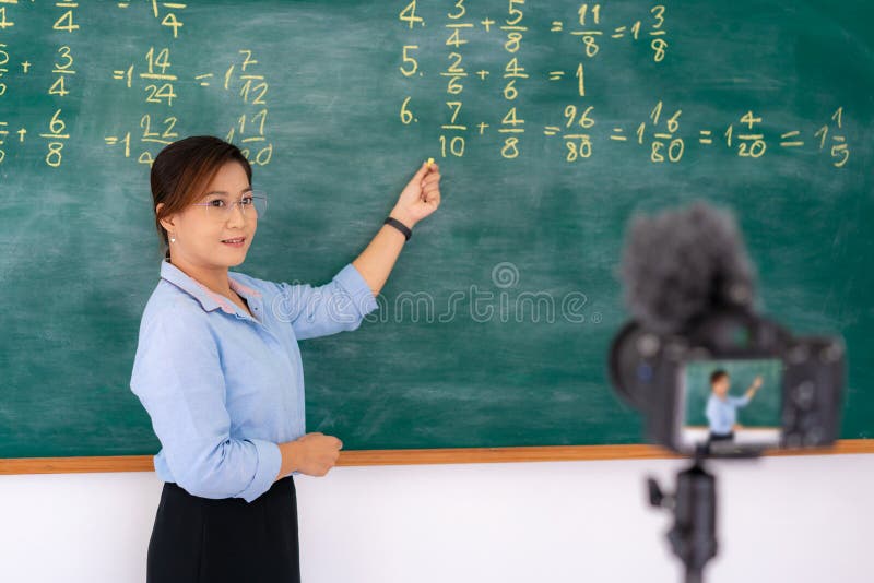 Asian primary teacher tutor explaining math in blackboard giving remote school class online lesson teaching looking at camera in royalty free stock image