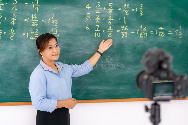 Asian primary teacher tutor explaining math in blackboard giving remote school class online lesson teaching looking at camera in stock photos