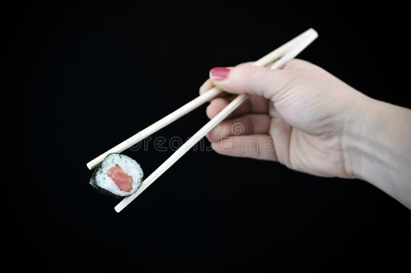 Asian Raw Fish Sushi Food in Chopsticks isolated on solid black background. Healthy dinner being held by the hand of a female model. Weight watchers stock images, royalty-free photos and pictures