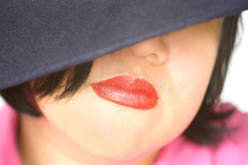 Full red lips and an Ecuadorian navy blue wool hat partly covering face of young asian woman. Suited for cosmetic, fashion, anonymous, undercover, fragrance, health, lifestyle, etc layout. Full red lips and an Ecuadorian navy blue wool hat partly covering face of young asian woman. Suited for cosmetic, fashion, anonymous, undercover, fragrance, health, lifestyle, etc layout.