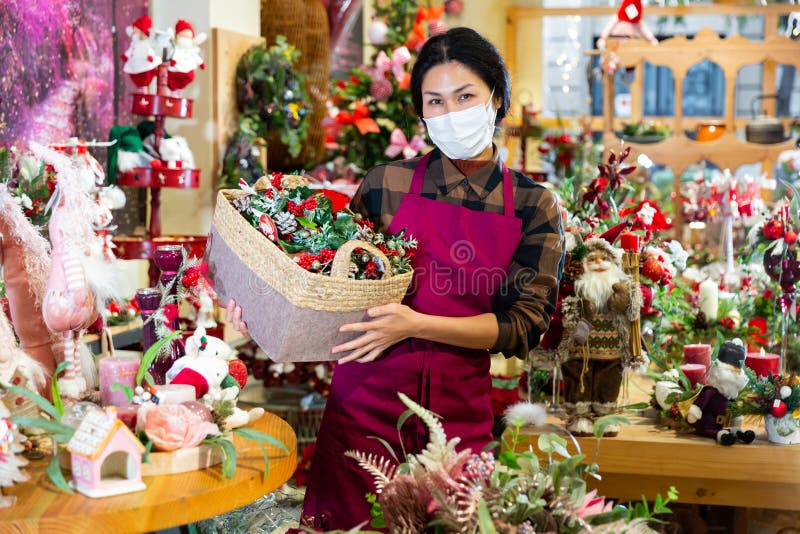 Asian saleswoman in face mask selling Christmas decorations at shop for decor. Asian saleswoman in face mask selling Christmas decorations at shop for decor