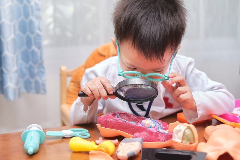 Asian school boy in doctor uniform playing doctor at home, kid wearing stethoscope learning and play with anatomical body organs