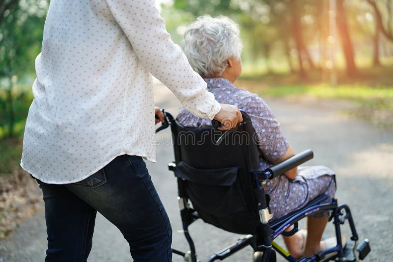 Asian senior or elderly old lady woman patient with care, help and support on wheelchair in park in holiday