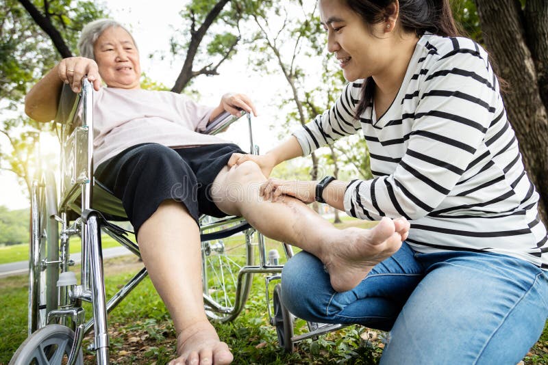 Asian senior mother in wheelchair,receiving a leg massage from her daughter,old woman enjoy,pain relief,elderly people suffer from