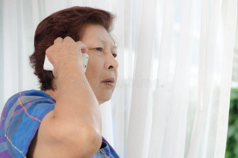 Asian senior woman using a phone call near window at home..