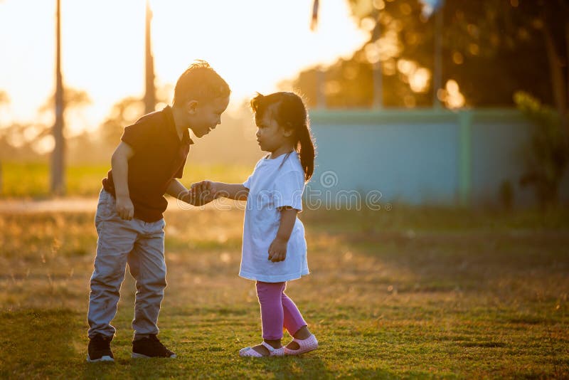 Asian siblings big brother and young sister holding hand and playing in the park together at sunset time