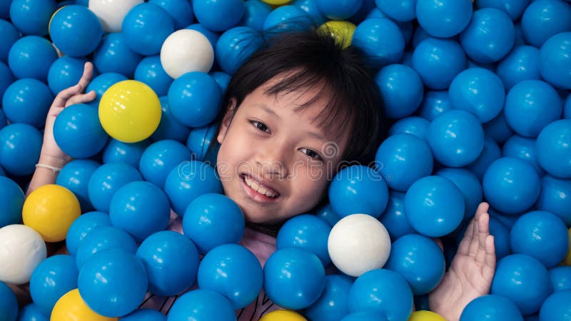 Asian smiling child girl playing lying in colorful balls park playground.16:9 style