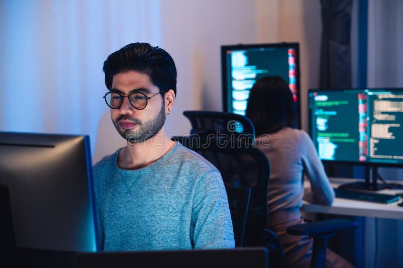 Asian software developers working on multiple screens displaying code and application diagrams at night in modern office stock photo