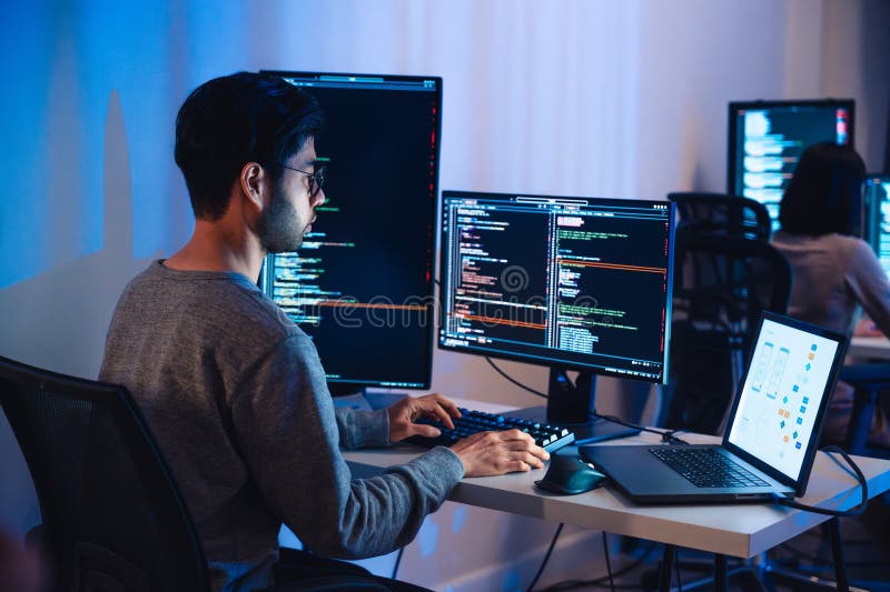 Asian software developers working on multiple screens displaying code and application diagrams at night in modern office royalty free stock photography