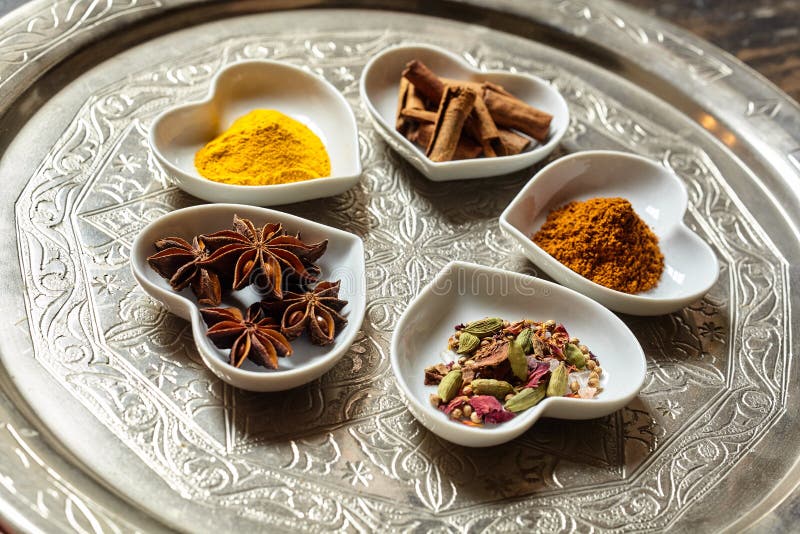 Various culinary asian spices ground or shredded in little piles within white heart shaped dishes over ornate silver platter and wood background. Various culinary asian spices ground or shredded in little piles within white heart shaped dishes over ornate silver platter and wood background