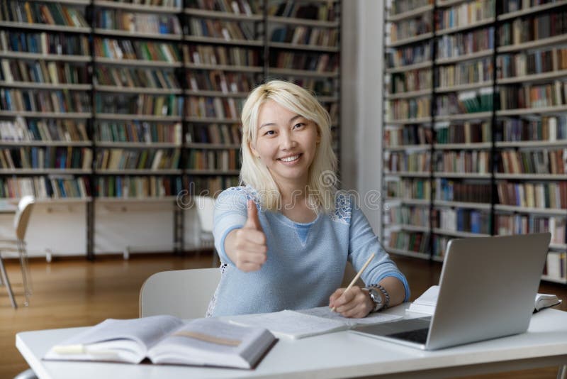 Asian Student Shows Thumbs Up Seated at Table in Library Stock Photo ... photo