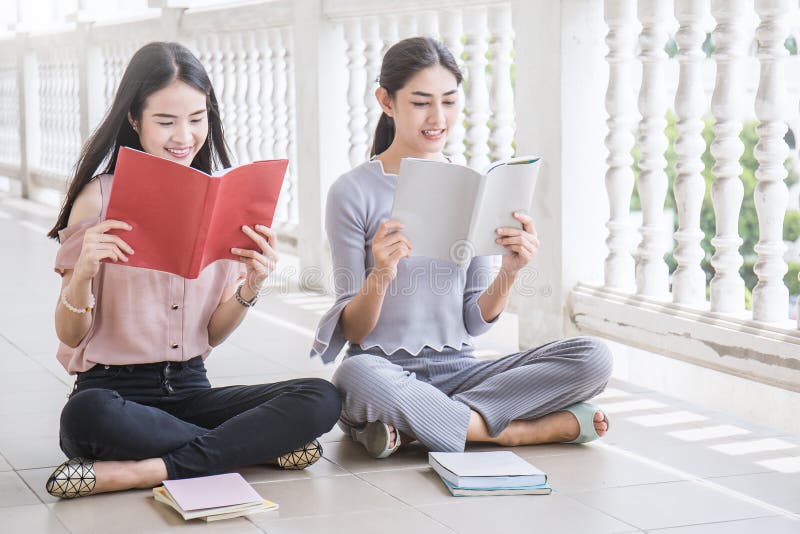 Asian student sitting outside school building reading book