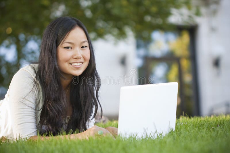 Atraktivní Asijské student studuje venku na její přenosný počítač.