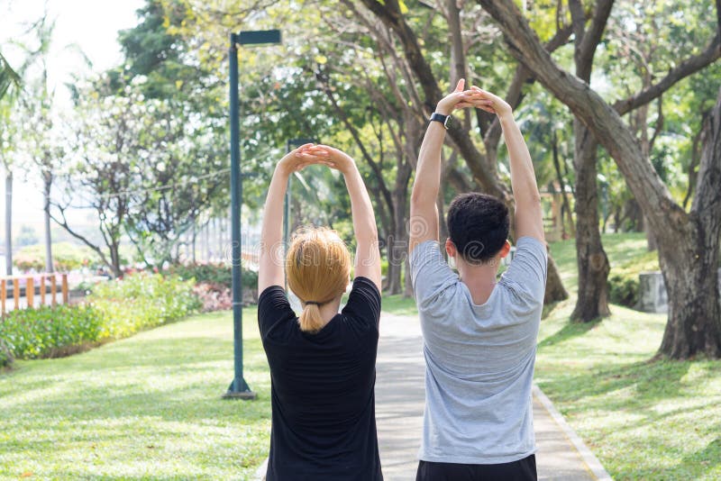 Asian sweet couple warm up their bodies by stretching arms before morning jogging exercise in the park.