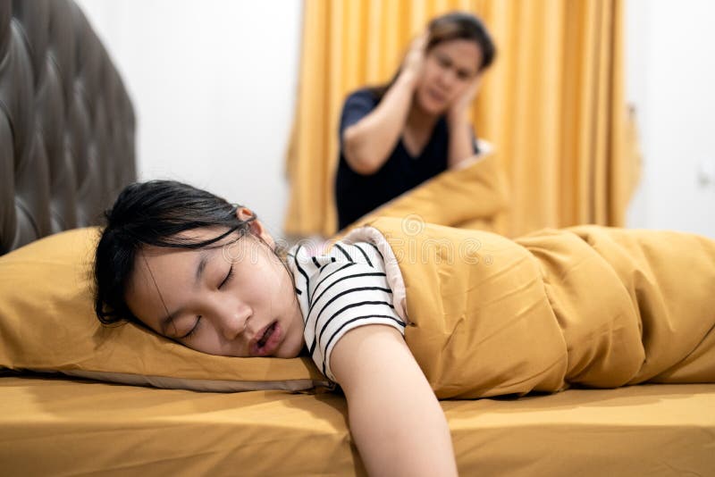 Asian teenage girl snoring loudly,open mouth,drooling on pillow,feeling tired exhausted,unhappy women or mother covering ears with both hands,annoyed by the snoring of child girl,danger of sleep apnea. Asian teenage girl snoring loudly,open mouth,drooling on pillow,feeling tired exhausted,unhappy women or mother covering ears with both hands,annoyed by the snoring of child girl,danger of sleep apnea