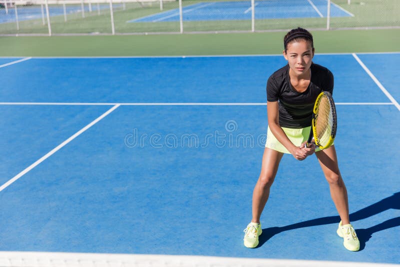 Asian tennis player woman ready to play on blue hard court outdoor in summer in position holding racket wearing outfit with skirt and shoes. Female athlete determination and concentration concept. Asian tennis player woman ready to play on blue hard court outdoor in summer in position holding racket wearing outfit with skirt and shoes. Female athlete determination and concentration concept