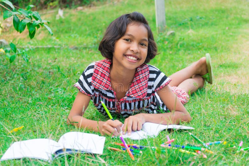 Asian Thai girl lying on the grass with colored pencil and homework book from school with happy expression