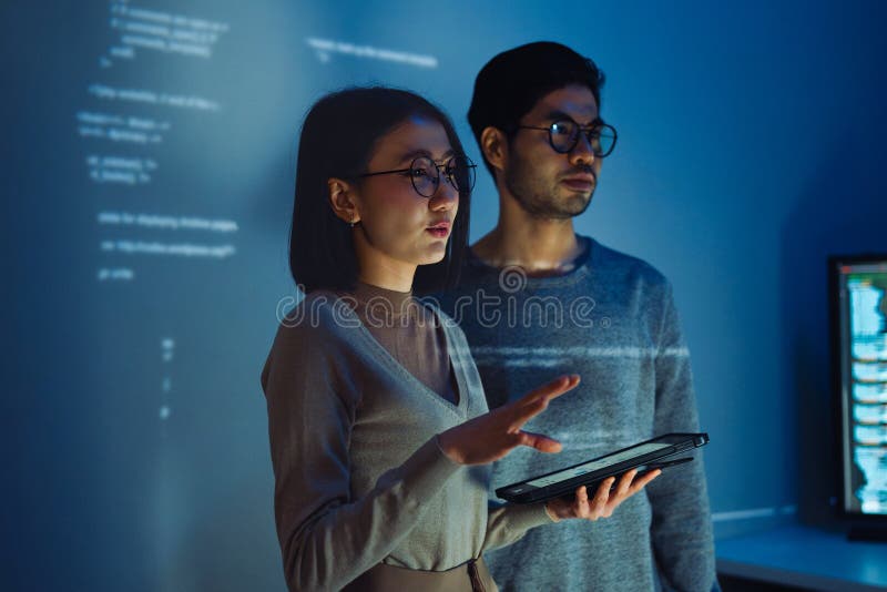 Asian Two software developers engaged in collaborative coding session, with code projected onto the wall and multiple computer royalty free stock photo