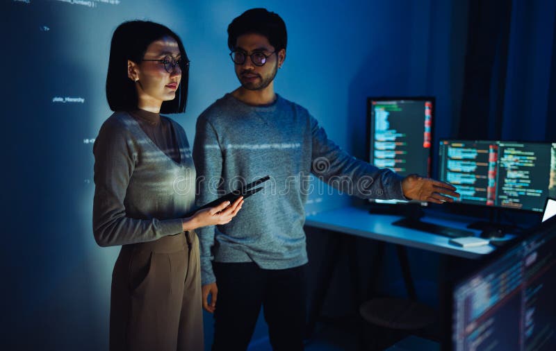Asian Two software developers engaged in collaborative coding session, with code projected onto the wall and multiple computer stock photography