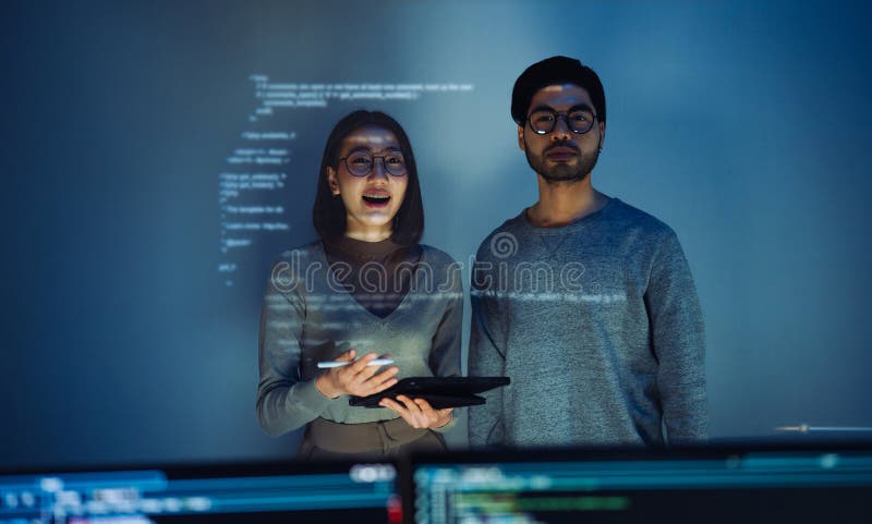 Asian Two software developers engaged in collaborative coding session, with code projected onto the wall and multiple computer royalty free stock photography