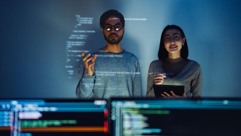 Asian Two software developers engaged in collaborative coding session, with code projected onto the wall and multiple computer stock photos