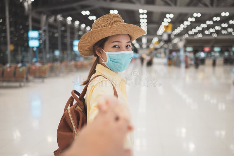 Asian woman backpacker wearing protective face mask raise up hand to holding hand with couple in an international airport