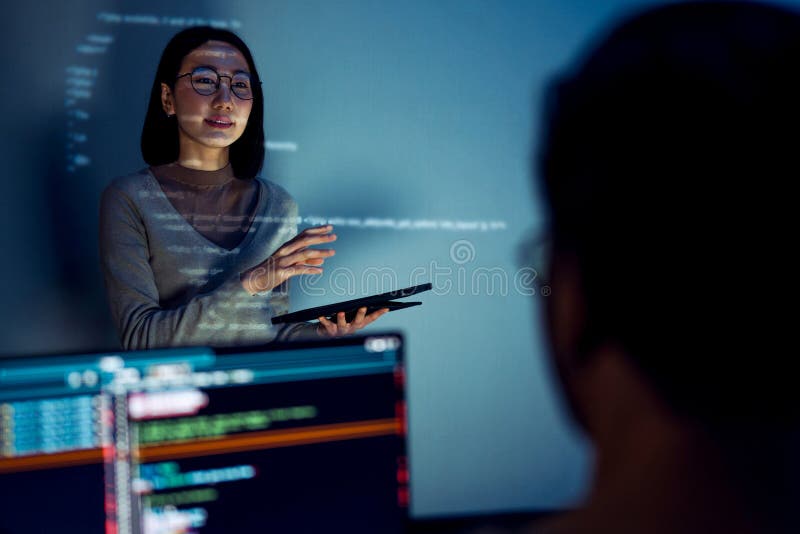 Asian woman developers collaborating on a coding project, with one member presentation at code projected on the wall while the stock image