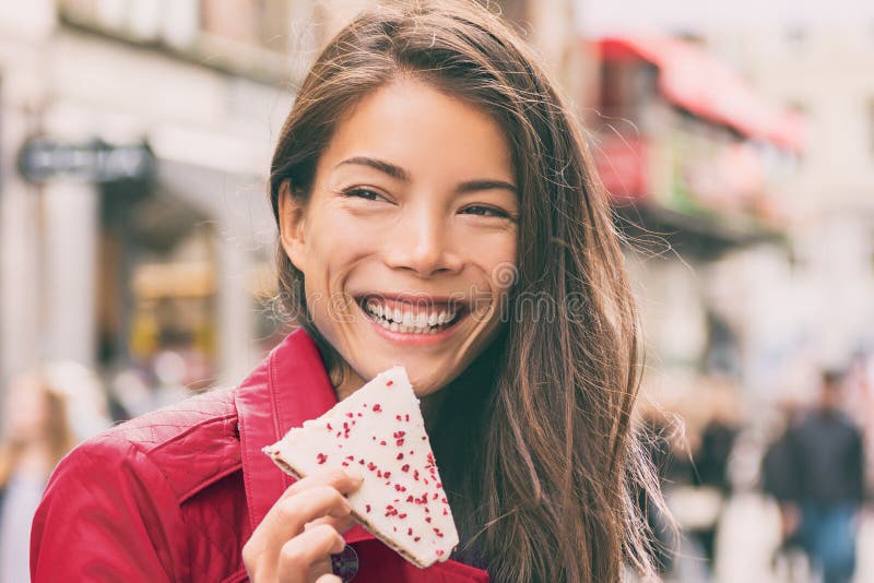 Asian woman eating cookie in city street happy smiling. Girl holding a hindbaersnitte raspberry cake enjoying urban lifestyle. royalty free stock photography Asian woman eating cookie in city street happy smiling. Girl holding a hindbaersnitte raspberry cake enjoying urban lifestyle. royalty free stock photography