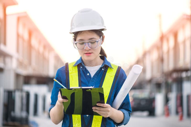 Asian woman engineer or architecture hold clipboard standing face to camera at construction site and checking audit checklist.