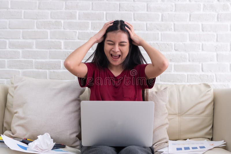 Asian woman freelancer shout with stress emotion while working with laptop and paperwork at sofa in living room in house. royalty free stock photo Asian woman freelancer shout with stress emotion while working with laptop and paperwork at sofa in living room in house. royalty free stock photo