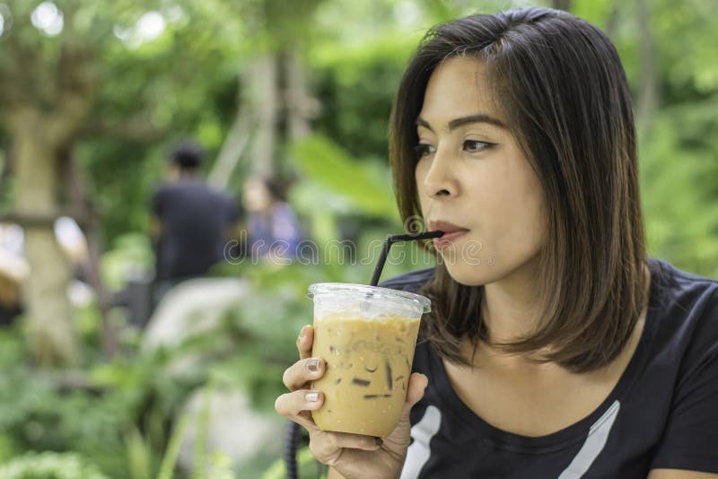 Asian woman holding a glass of cold espresso coffee Background blurry views tree royalty free stock photo Asian woman holding a glass of cold espresso coffee Background blurry views tree royalty free stock photo