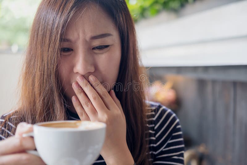 Asian woman holding hot coffee with feeling strange and smelling bad in coffee shop