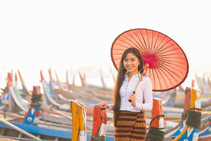 An Asian woman holding a red umbrella with a gondola. A young Burmese woman with a red umbrella on wooden boat at bridge in Asia.U