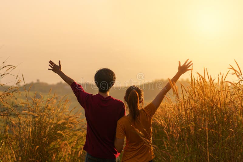 Asian woman and man standing and hand up in meadow and looking far away at sunrise time