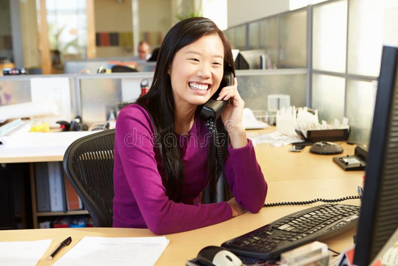 Asian Woman On Phone In Busy Modern Office Smiling On Telephone