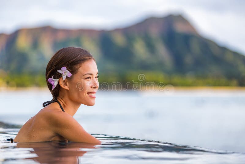 Asian woman relaxing in infinity pool at luxury spa resort in Hawaii, watching ocean beach from hotel. Girl tourist on travel vacation in Waikiki, Honolulu, USA holiday. Summer outdoor wellness.