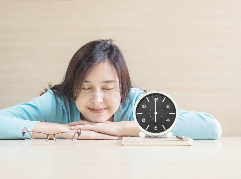 Asian woman sleep by lied on desk with happy face in rest time from reading book with clock show the time in 6 o`clock on desk.