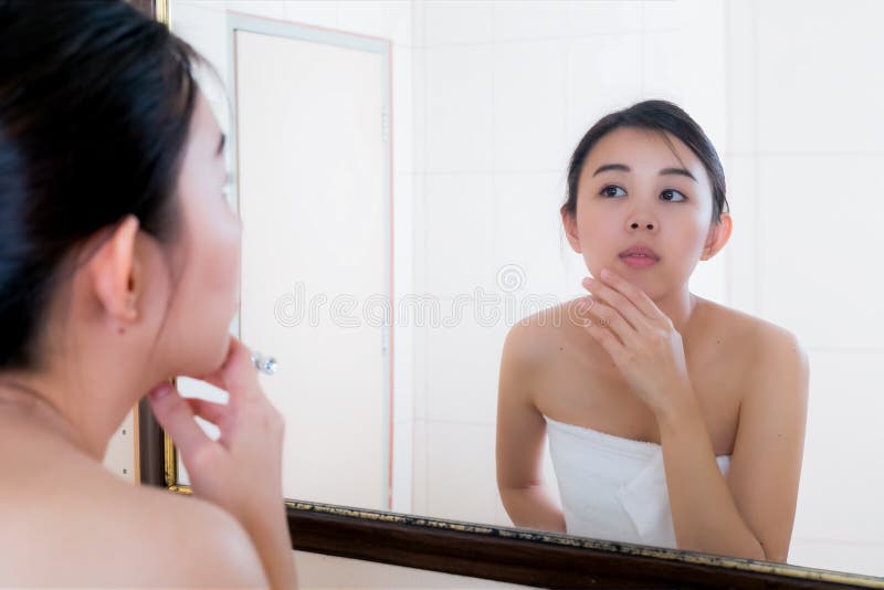 Asian woman squeezing pimples on her face while looking at reflection in mirror. royalty free stock photo Asian woman squeezing pimples on her face while looking at reflection in mirror. royalty free stock photo
