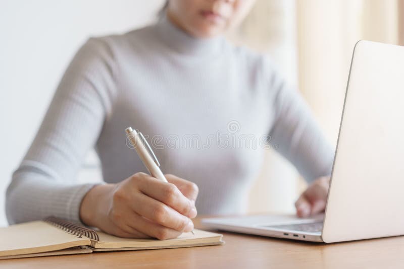 Asian woman is taking notes and using  laptop computer at office