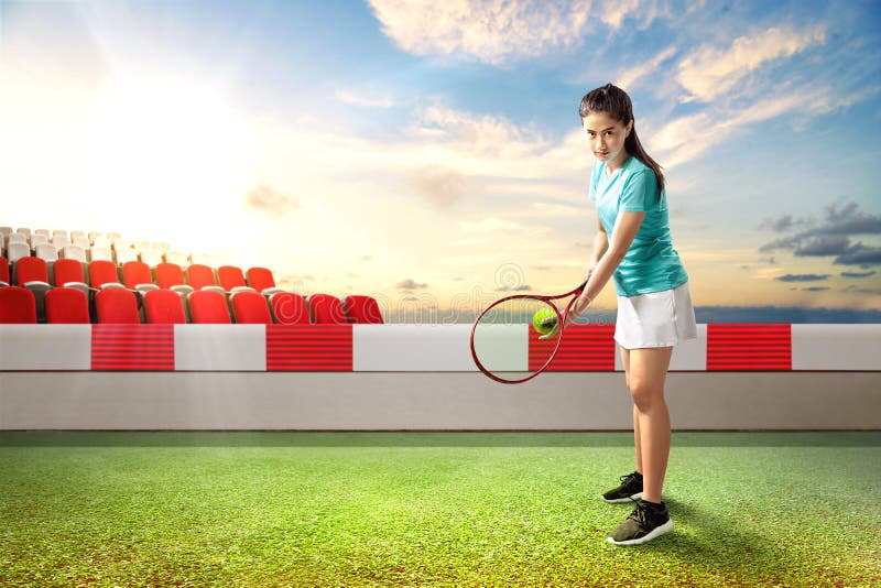 Asian woman with a tennis racket and ball in her hands ready in serve position