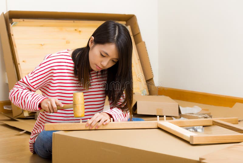 Asian woman using hammer for furniture assembling stock photography