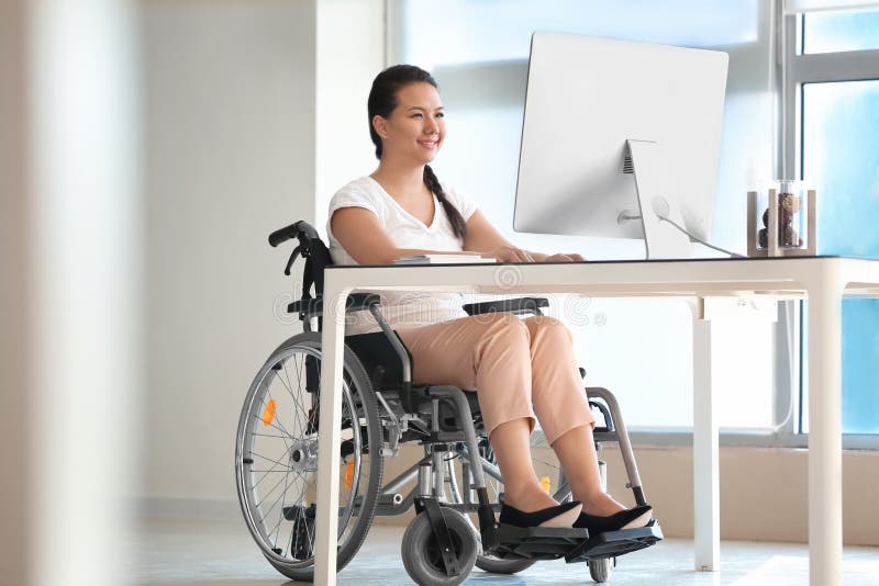 Asijský žena v invalidní vozík pracovní počítač v kancelář.