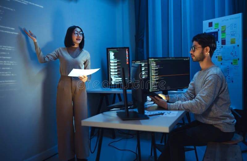 Asian woman developers collaborating on a coding project, with one member presentation at code projected on the wall while the stock image