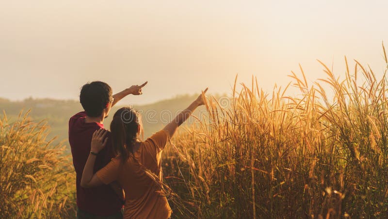 Asian woman and man standing and point hand in meadow and looking far away at sunrise time